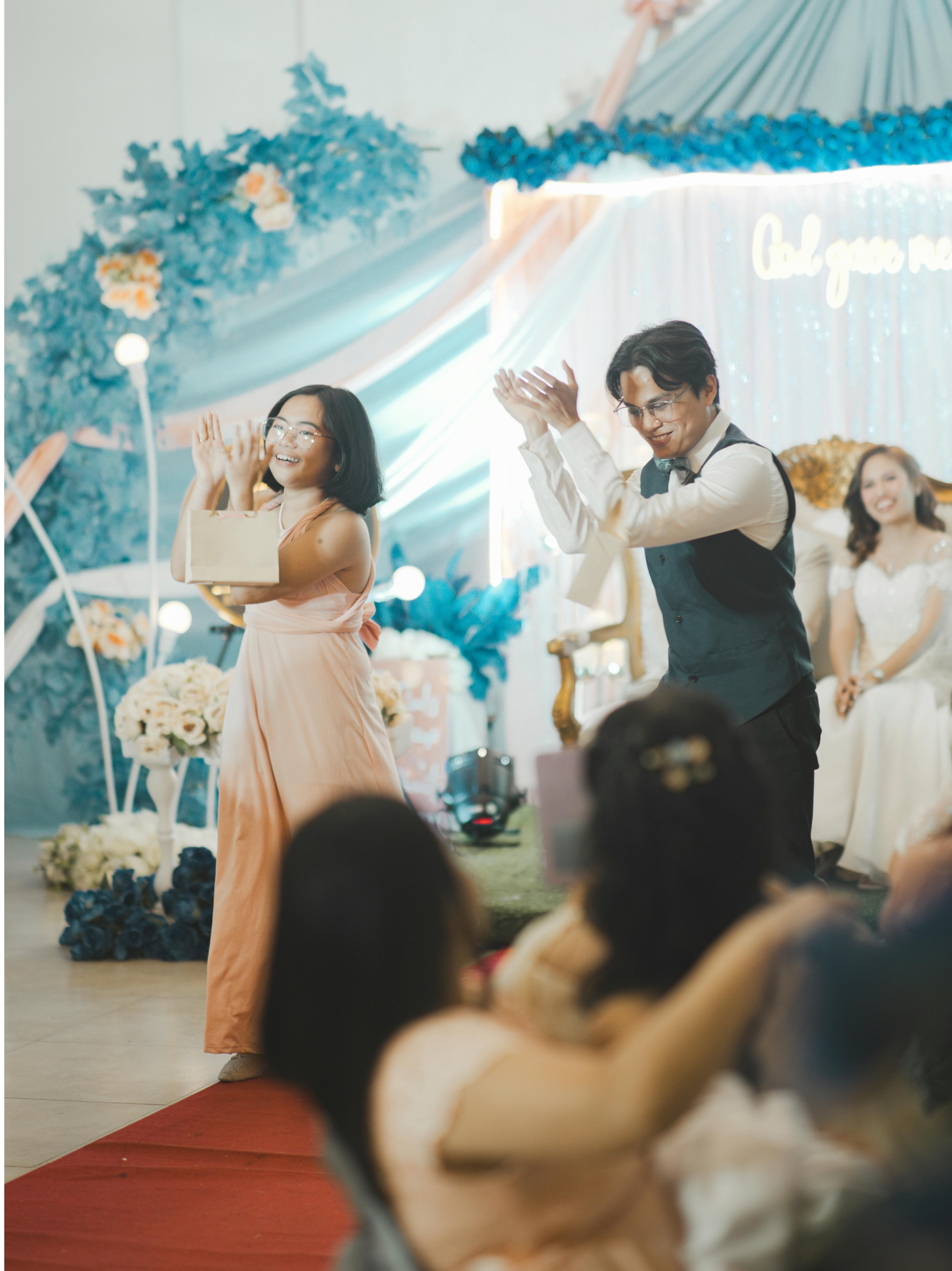 Two BIPOC people - one woman in a pink dress and one man in a black vest dance together at a wedding party.